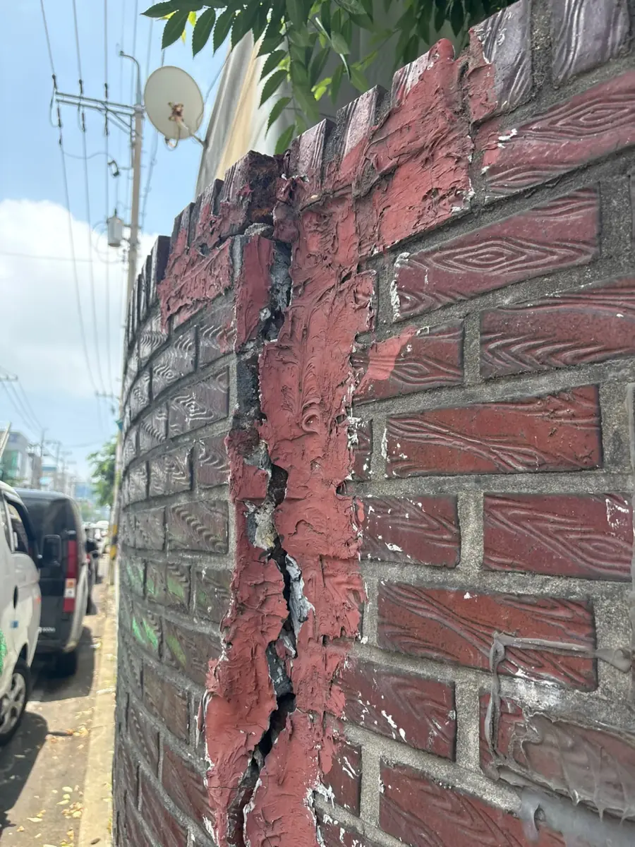 수직 균열이 벌어진 벽돌 담벼락 상태 사진